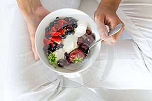 Healthy eating concept. Women`s hands holding bowl with cottage cheese with cream, strawberry, cherry, gooseberry and blueberry