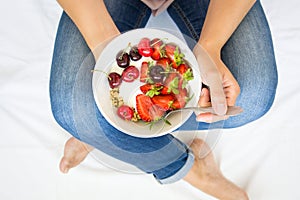 Healthy eating concept. Women`s hands holding bowl with muesli, yogurt, strawberry and cherry. Top view. Lifestyle