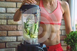 Close up of young woman with blender and green vegetables making detox shake or smoothie at home