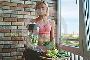 Close up of young woman with blender and green vegetables making detox shake or smoothie at home