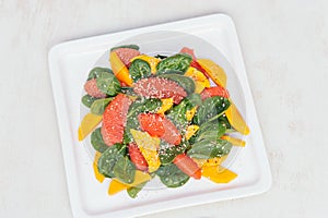 Healthy eating and dieting concept. Fresh salad of mango, grapefruit, spinach and hempseed on white square plate. Top view.