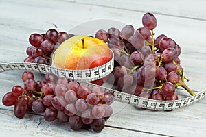 Healthy eating and fitness concept - apple, grapes and measuring tape