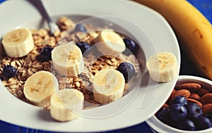 Healthy eating, food and diet concept - oatmeal with berries, nuts and bananas, white plate, blue wooden background.