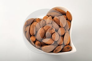 Healthy eating habits and heart healthy foods concept with a heart shaped bowl filled with almonds isolated on white background