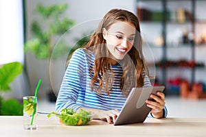 Healthy eating. happy young girl eating salad with tablet pc in morning in kitchen
