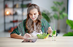 Healthy eating. happy young girl eating salad with tablet pc in morning in kitchen