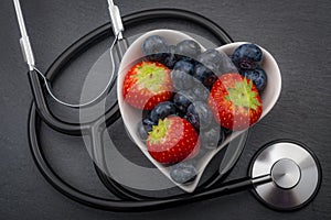 Healthy eating and heart health concept with a heart shaped bowl with blueberries and a stethoscope each blueberry is packed full