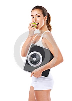 Healthy eating is the key. a young woman eating an apple while holding a scale.