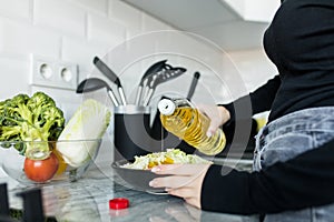 Healthy eating, vegetarian food, dieting and people concept - close up of young woman dressing vegetable salad with oil at home