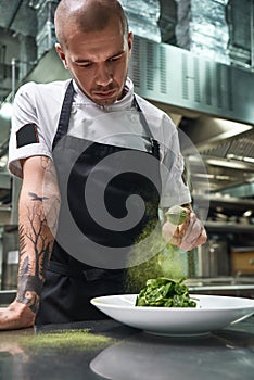 Healthy eating. Vertical portrait of handsome male chef in black apron adding spices in salad