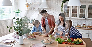 Healthy eating. Young beautiful family cooking together in the modern kitchen at home. Mother and father teaching two