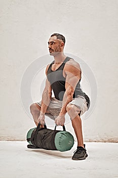 Healthy and energetic man doing squats with a sand bag looking strong