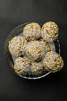 Healthy energy balls with sesame in glass bowl on black background