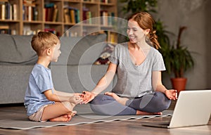 Healthy family mom and son meditating together at home while having online yoga class on laptop