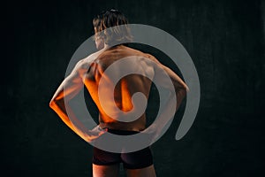 Healthy fit relief ack. Rear view of young shirtless man with muscular body standing in underwear against dark textured