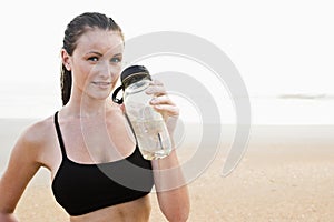 Healthy fit young woman on beach drinking water