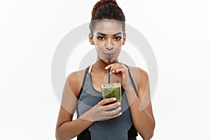 Healthy and Fitness concept - Beautiful American African lady in fitness clothing drinking healthy vegetable drink