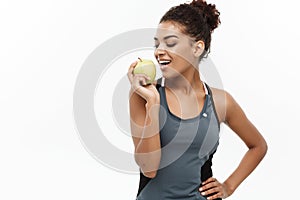 Healthy and Fitness concept - Beautiful American African lady in grey fitness clothes eating green apple. Isolated on