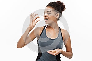 Healthy and fitness concept - closeup portrait of beautiful African American taking a pill of cod liver oil. Isolated on