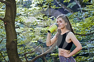 Healthy fitness girl drinking water from green bottle in forest