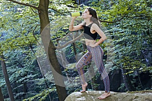 Healthy fitness girl drinking water from green bottle in forest