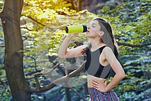 Healthy fitness girl drinking water from green bottle in forrest