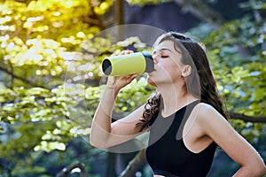 Healthy fitness girl drinking water from green bottle in forrest