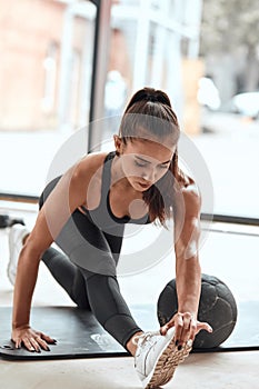 Healthy, fitness lifestyle. Fit woman in sportsuit stretching legs with medicine ball at gym
