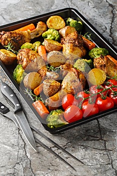 Healthy food baked chicken drumstick with broccoli, potatoes, tomatoes and carrots close-up on a sheet pan. Vertical
