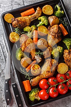 Healthy food baked chicken drumstick with broccoli, potatoes, tomatoes and carrots close-up on a sheet pan. Vertical top view