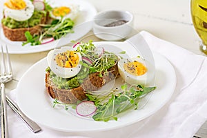 Avocado egg sandwich with whole grain bread on white wooden background