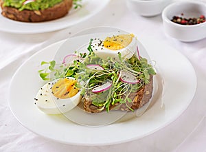 Avocado egg sandwich with whole grain bread on white wooden background