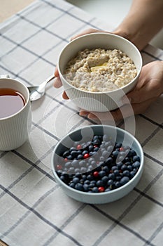 Healthy food breakfast with oatmeal porridge in bowl with summer berries, slice of butter, mug tea.