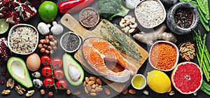 Healthy food clean eating selection: fish, fruit, nuts, vegetable, seeds, superfood, cereals, leaf vegetable on black concrete