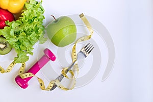 Healthy food clean eating selection with fruits, vegetables, dumbbell and tape measure on white table background. Organic food,