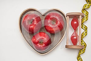 Healthy Food Concept. Diet and Fitness. Glass Clock and Red Apple in Heart Shape Wooden Box. Measuring Tape, isolated on white bac