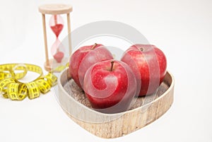 Healthy Food Concept. Diet and Fitness. Glass Clock and Red ripe Apple in Heart Shape Wooden Box. Cyan Measuring Tape, isolated on