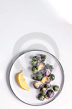 Healthy food concept, dieting, vegetarian, vegan - organic purple brussel sprouts fried on plate with lemon, top view