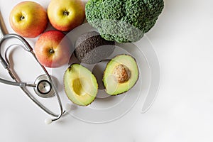 Healthy food concept. Fruit and vegetables and a statoscope laid out on a white background