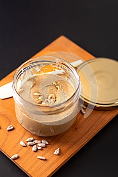 Healthy food concept homemake sunflower butter in glass jar by organic sunflower seeds on black background photo