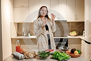 Healthy food concept. Young happy woman holding cherry tomato and smiling on background of modern white kitchen. Home cooking,