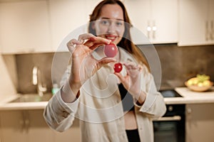 Healthy food concept. Young happy woman holding cherry tomato and smiling on background of modern white kitchen. Home cooking,