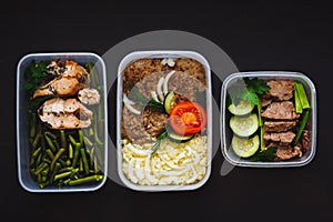 The healthy food in the containers on black background: snack, dinner, lunch. Baked fish, beans, beef cutlets, mashed potatoes, me