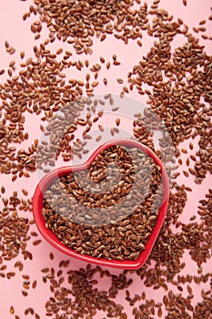 Healthy food. Flax seeds in red heart shaped bowls on pink background