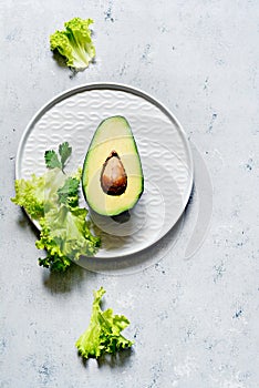 Healthy food. Half a ripe avocado with seed and lettuce on a plate on a gray background. Avocado salad Flat lay.