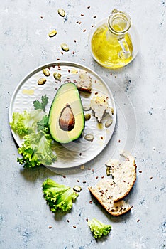 Healthy food. Half a ripe avocado with seed and lettuce on a plate on a gray background. Avocado salad Flat lay.