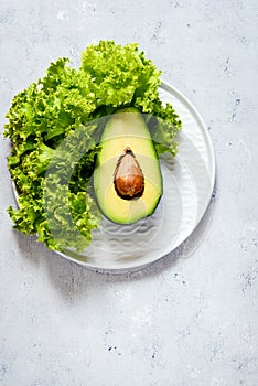 Healthy food. Half a ripe avocado with seed and lettuce on a plate on a gray background. Avocado salad Flat lay. Food concept.