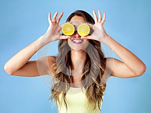 Healthy food is happy food. Studio shot of a young woman covering her eyes with oranges against a blue background.