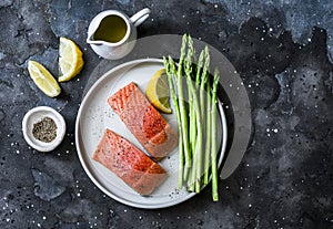 Healthy food ingredients - red fish salmon and fresh green asparagus on a dark background, top view