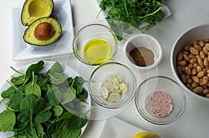 Healthy food ingredients used to prepare a delicious dip, including avocado, olive oil, garlic, cumin, pink salt, beans, spinach,